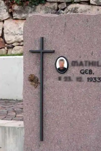 kleines Bronzekreuz mit Rose gibt dem Grabstein eine persönliche Note